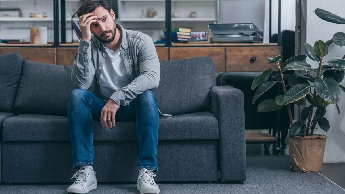 Mann sitzt nachdenklich auf Sofa – sitzender Lebensstil als Risikofaktor fuer Akne im Erwachsenenalter