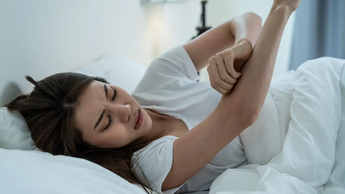 Frau kratzt sich nachts im Bett am Arm als Symbol fuer chronischen Pruritus und dessen massive Belastung