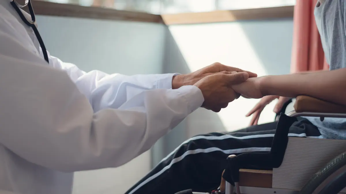 Arzt hält Hände eines neurologisch beeinträchtigten Kindes im Rollstuhl
