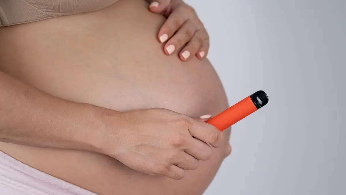 Schwangere hält einen orangefarbenen Vaper neben ihrem Bauch – Vapen in der Schwangerschaft ist gefährlich.