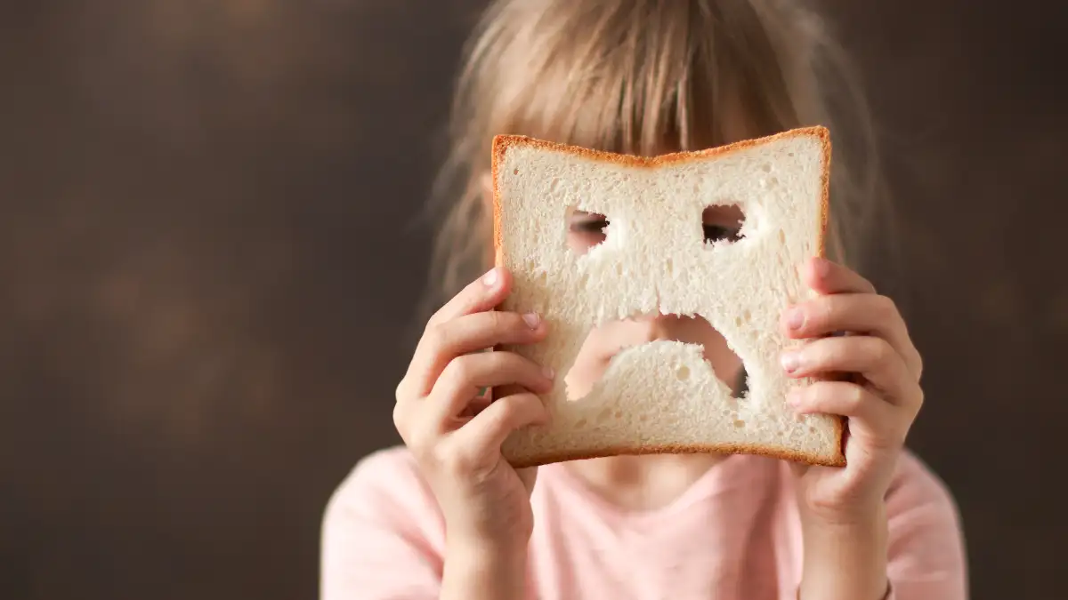 Ein Mädchen hält ein Toastbrot mit einem traurigen Smiley vor das Gesicht.