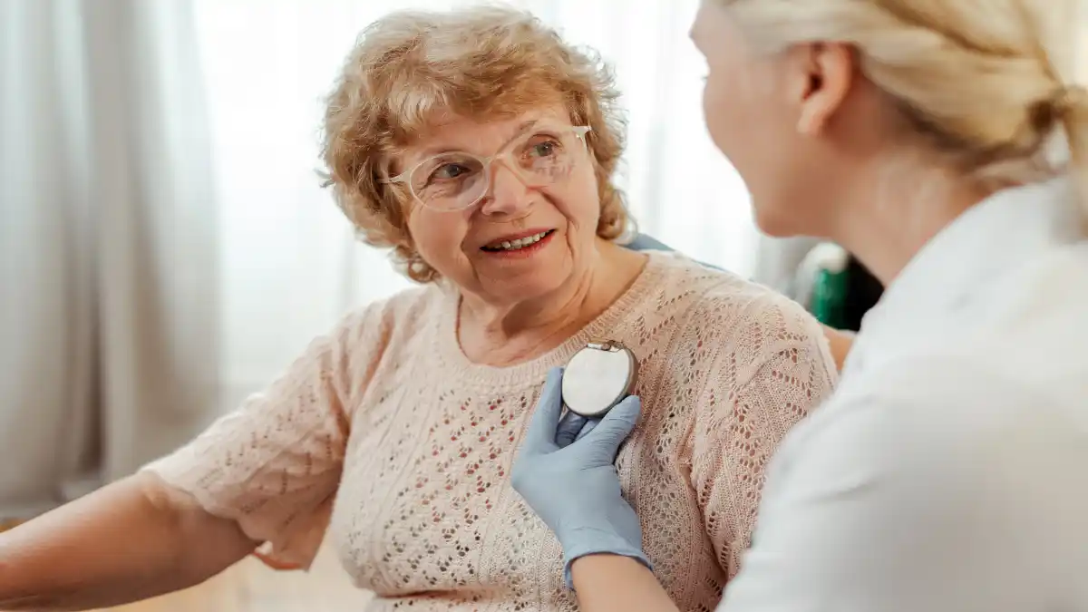 Auf diesem Foto sieht man eine junge Ärztin, die einen implantierbaren Kardioverter-Defibrillator an die Brust einer älteren Dame hält.