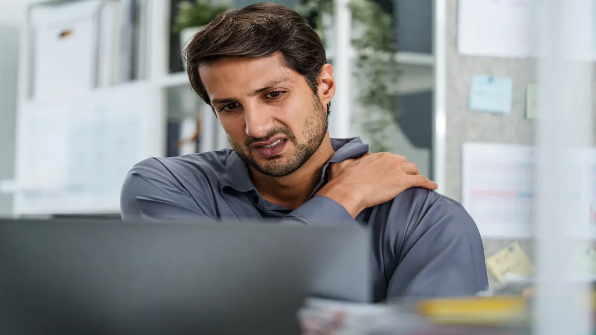 Frozen Shoulder Symptome bei Mann am Laptop