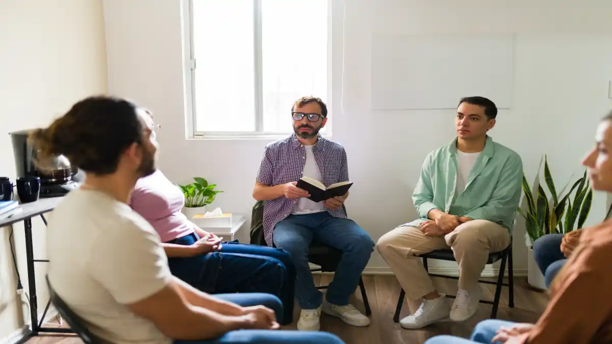 Auf dem Bild ist ein Gruppentherapiesetting dargestellt, Menschen sitzen im Kreis auf Stühlen.