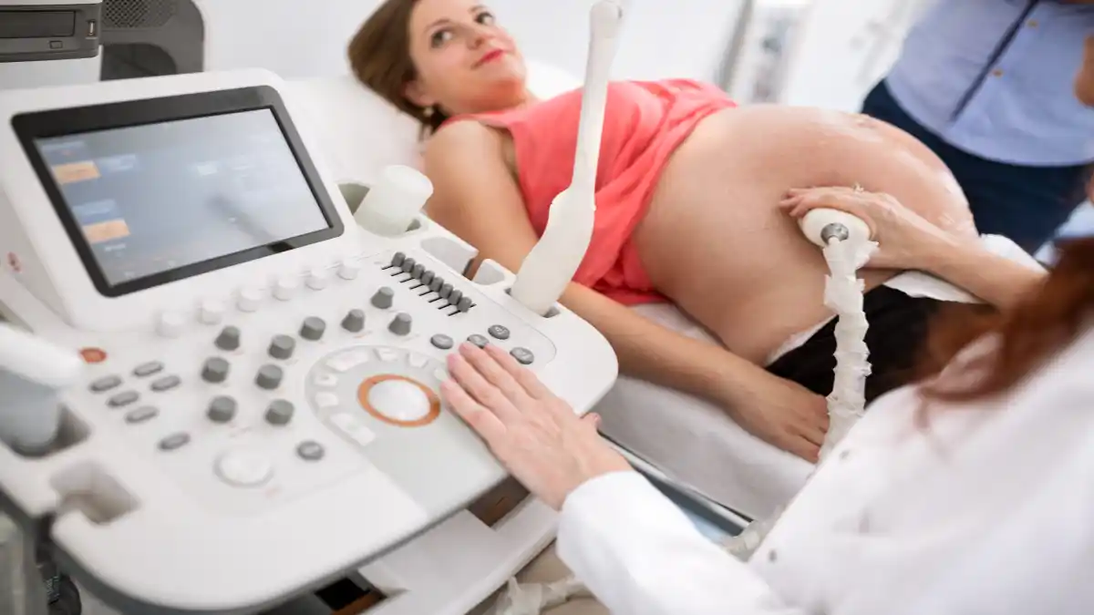 Eine schwangere Frau blickt auf den Ultraschallmonitor während eine Ärztin den Ultraschall durchführt.