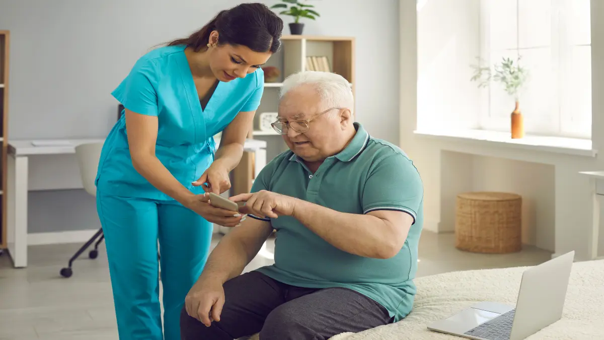 Pflegerin zeigt älterem männlichen Patienten eine digitale Anwendung auf dem Smartphone