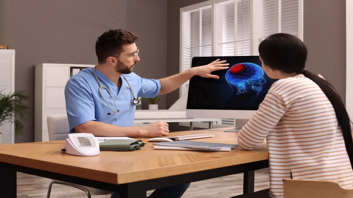 Arzt erklärt Patientin einen Hirntumor anhand einer 3D-Gehirndarstellung auf dem Computerbildschirm