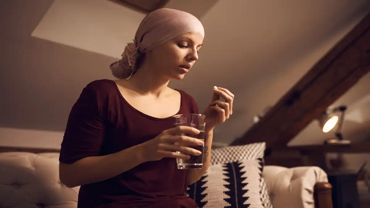 Eine junge Frau mit Krebs mit eine Tuch über dem haarlosen Kopf nimmt eine Tablette.