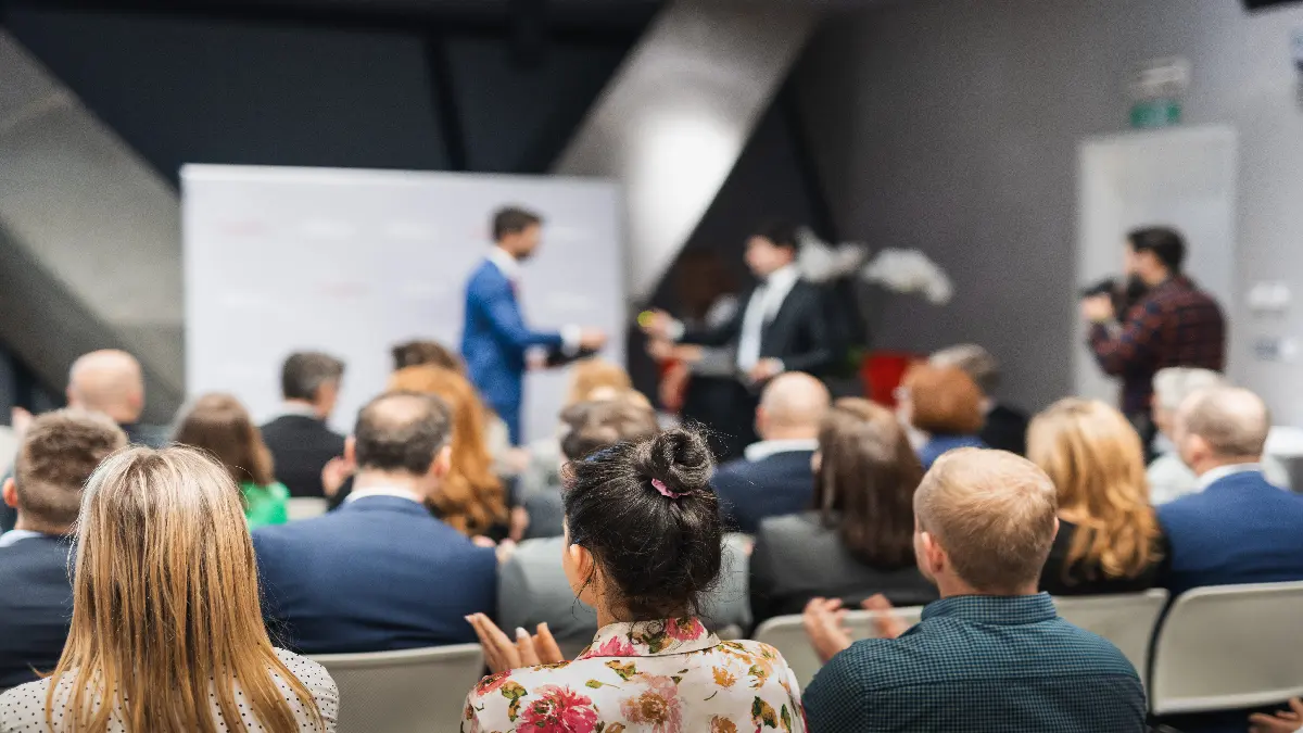 Publikum bei einer Konferenz waehrend ein Vortrag auf der Buehne gehalten wird