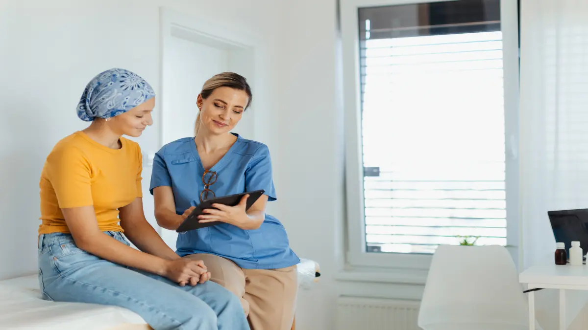 Pflegeperson zeigt einer Krebspatientin Informationen auf einem Tablet in einem hellen Behandlungszimmer