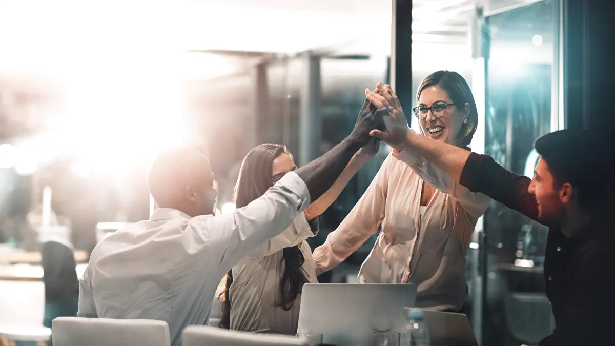 Vier Teammitglieder geben sich gemeinsam einen High-Five im Büro und feiern einen gemeinsamen Erfolg