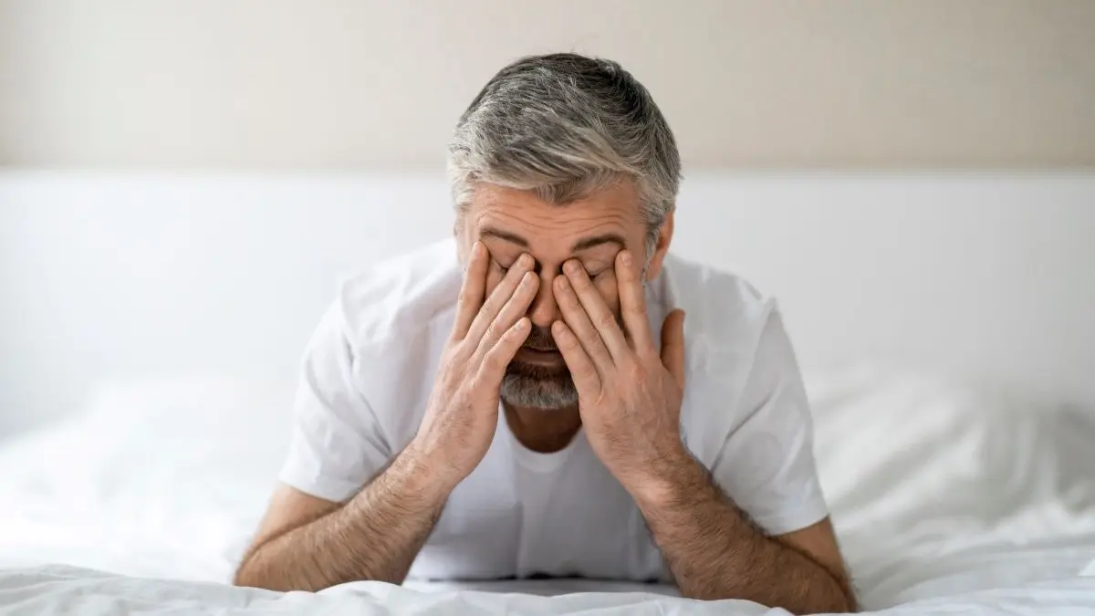 Person sitzt erschöpft im Bett und reibt sich die Augen als Symbol fuer muedigkeit und unspezifische Symptome bei Testosteronmangel