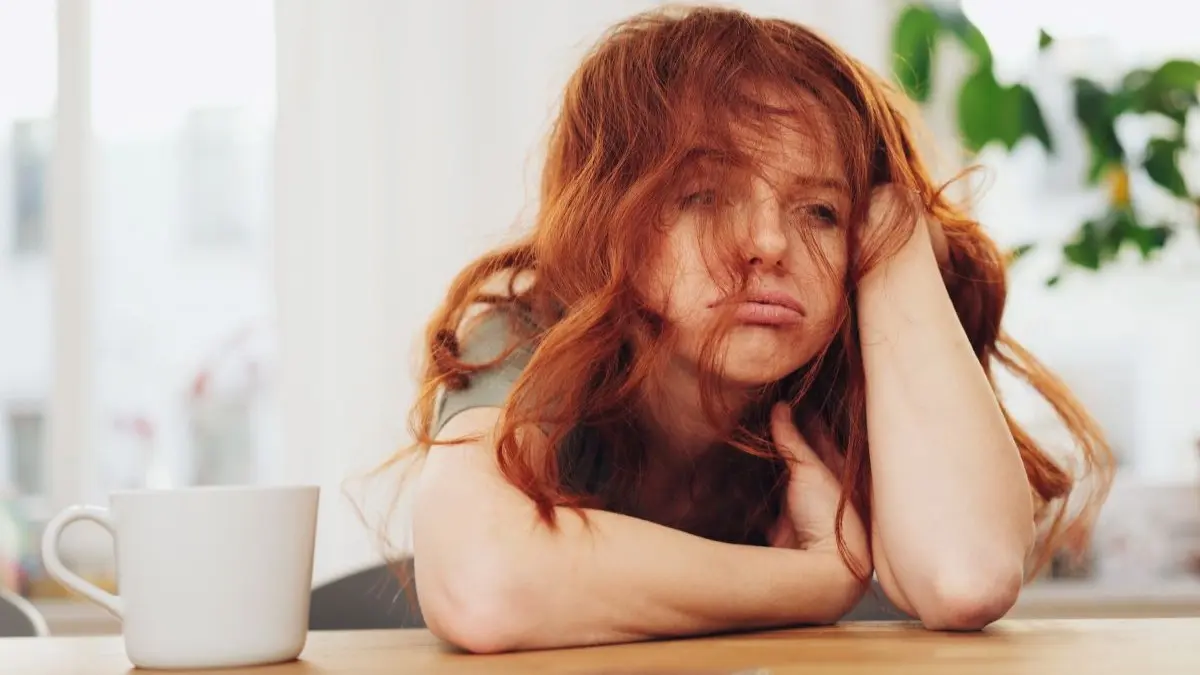 Erschoepfte junge Frau am Tisch, Symbolbild fuer Nährstoffbedarf und Vaginalflora unterstuetzen