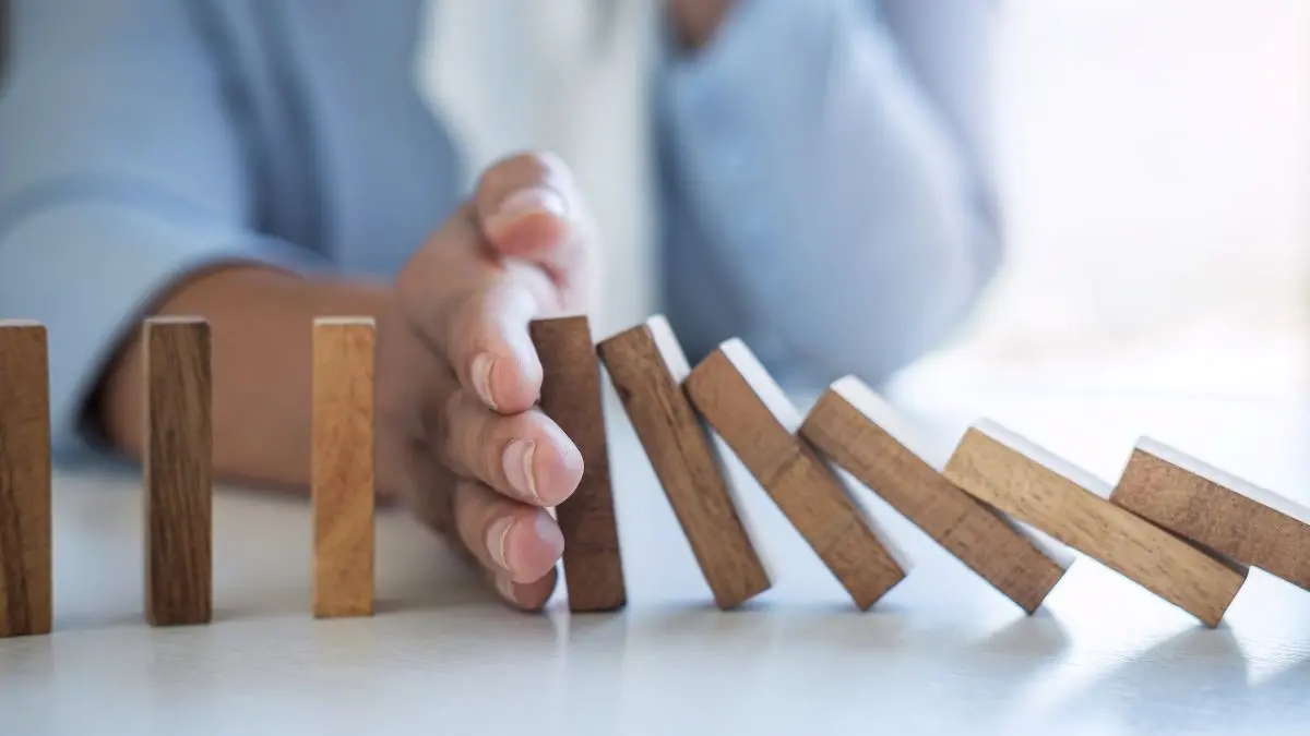 Hand stoppt fallende Holzsteine in einer Domino-Reihe, Symbolbild fuer rechtssicheren Umgang mit IGeL- und Selbstzahlerleistungen