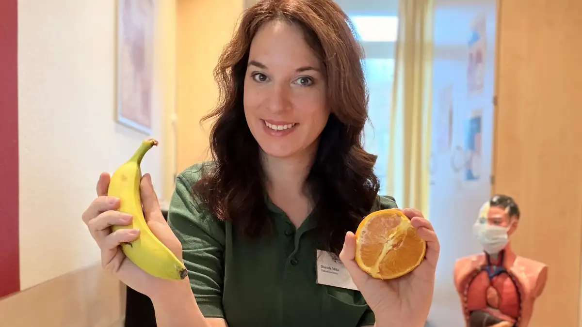 Diabetesberaterin Daniela Mika hält eine Banane und eine halbierte Orange in den Händen.