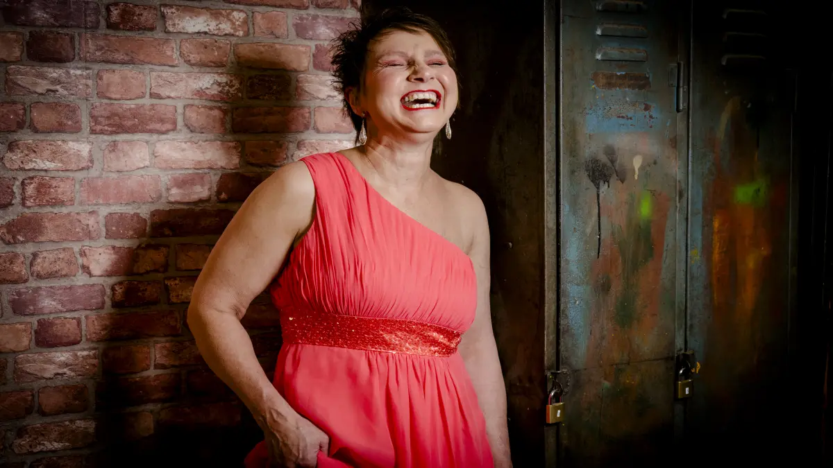 Frau in korallfarbenem Kleid lacht bei einem Mutmacher-Fotoshooting des Projekts unSICHTBAR