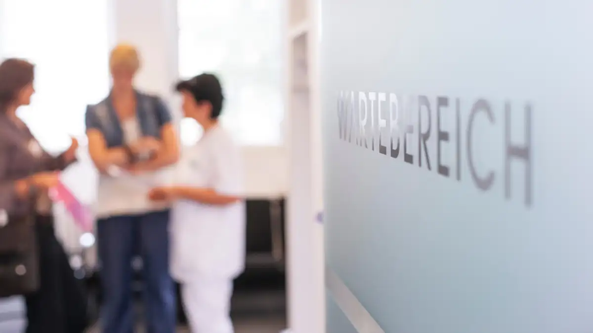 Blick ins Wartezimmer einer Arztpraxis mit mehreren unscharfen stehenden Personen im Hintergrund