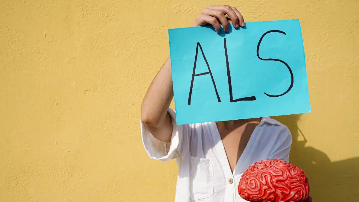 Person hält Schild mit Aufschrift „ALS" und ein Gehirnmodell – Symbol für Amyotrophe Lateralsklerose