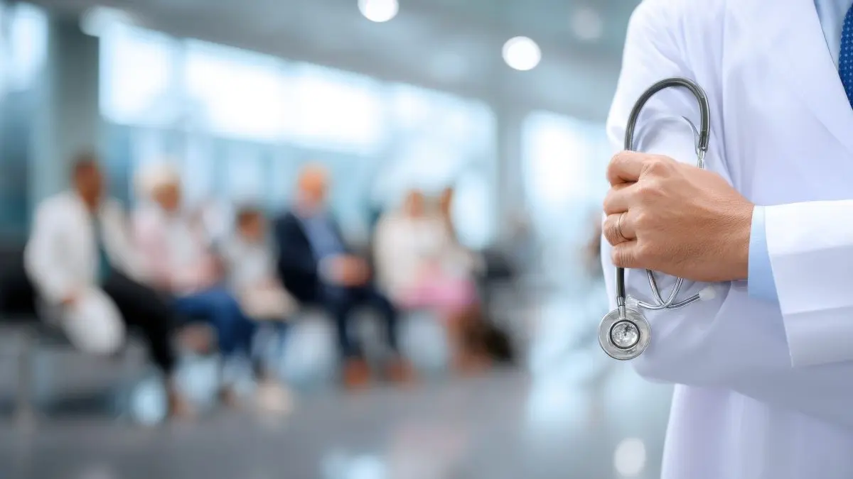 Arzt im weissen Kittel haelt Stethoskop vor einem unscharfen Wartezimmer mit vielen Patienten als Symbol dafuer, dass das Spargesetz der Regierung das Leistungsangebot reduzieren wird