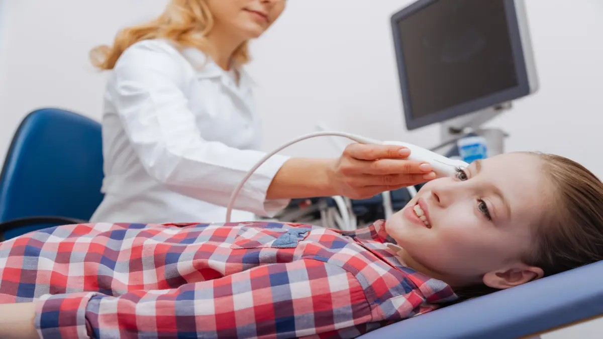 Ärztin führt Ultraschalluntersuchung am Kopf eines lächelnden Kindes in der Klinik durch