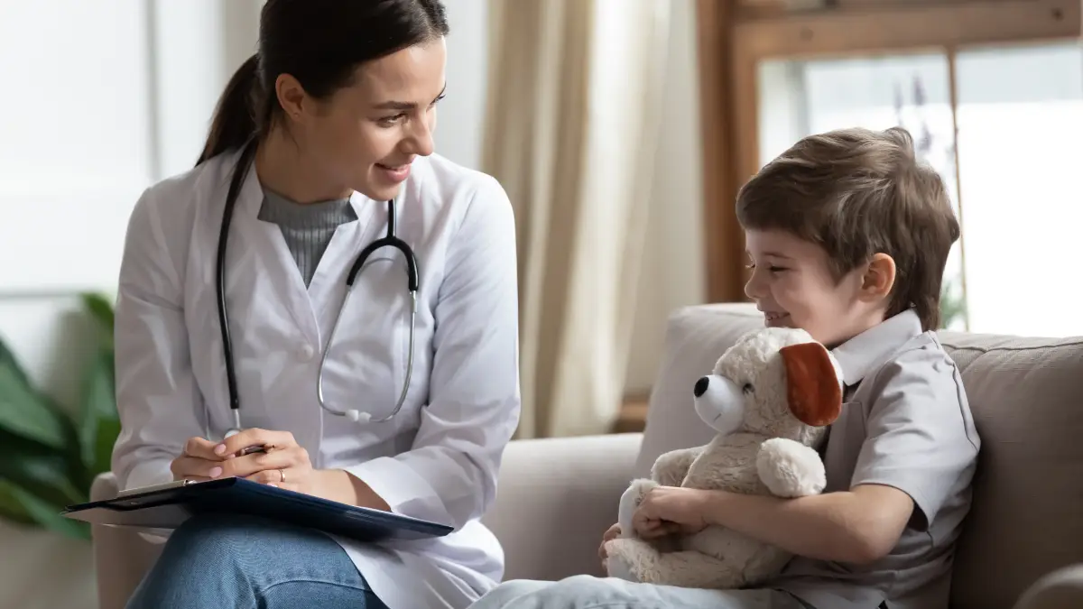 Kinderärztin spricht mit kleinem Jungen, der einen Teddybär hält