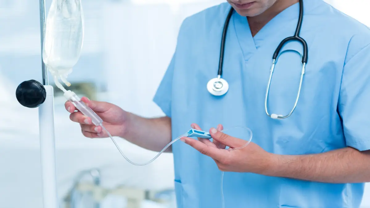 Arzt in blauem Kasack bereitet eine Infusion am Infusionsständer vor