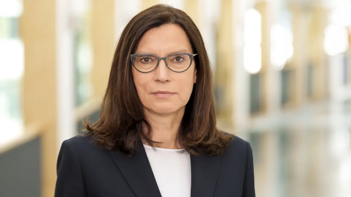 Portraet einer Frau mit Brille im Business-Outfit in einem hellen Klinik- oder Verwaltungsflur als Symbolbild fuer die Kritik der KBV an unzureichendem Buerokratieabbau in Arztpraxen
