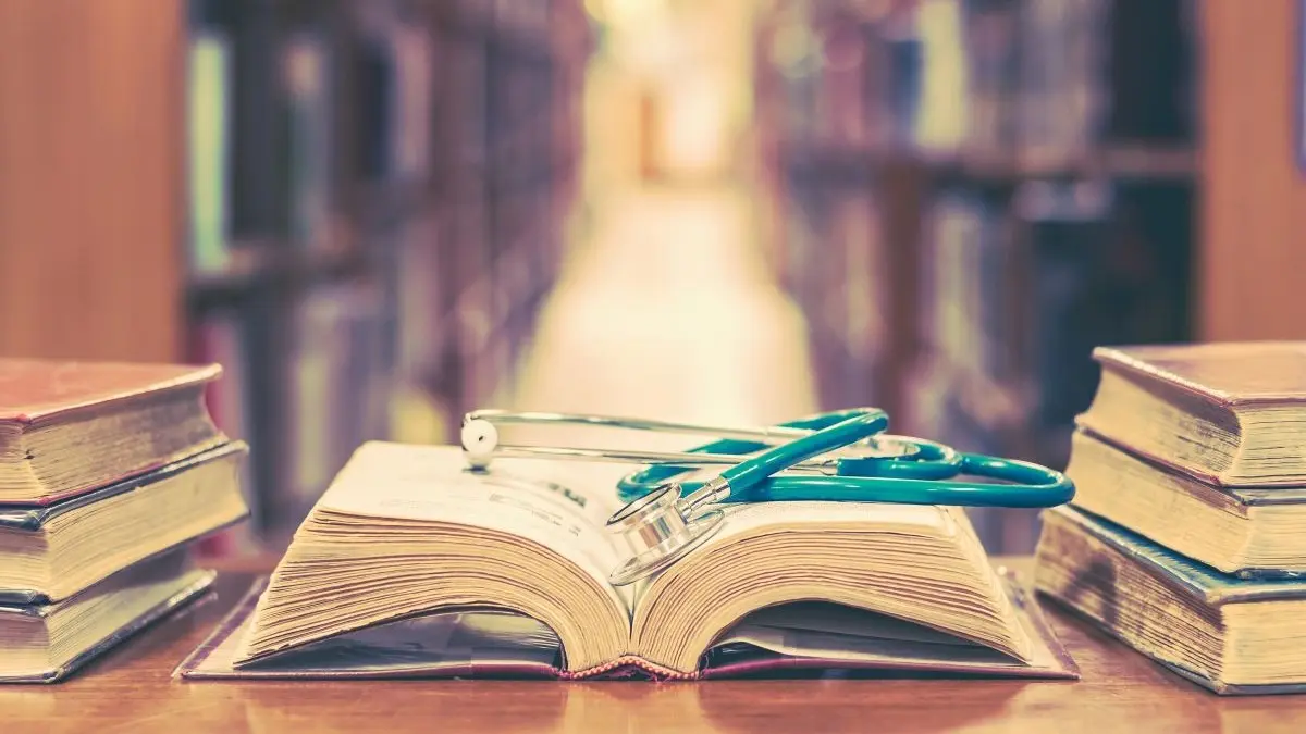 Offenes Buch mit Stethoskop in einer Bibliothek als Symbol fuer den Lesetipp Endstation Wartezimmer