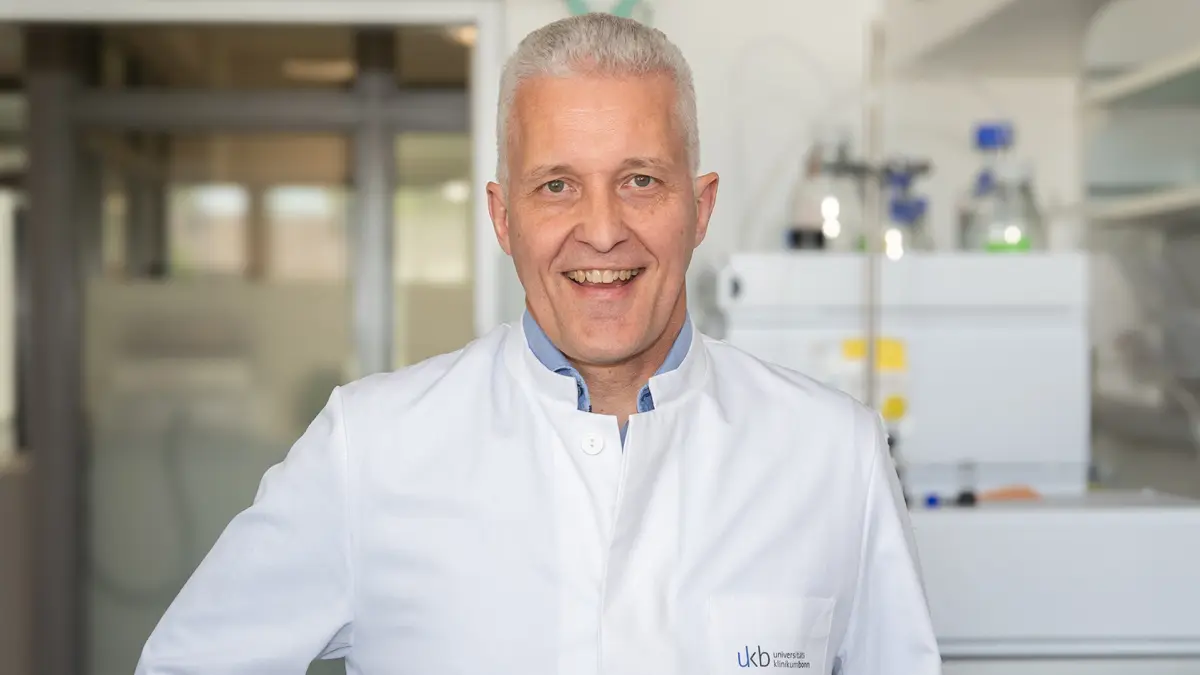 Laechelnder Forscher im weissen Kittel steht im Labor und symbolisiert neue Therapieansaetze gegen unkontrolliertes Tumorwachstum durch gezielte Hemmung von Cyclin-abhaengigen Kinasen CDK