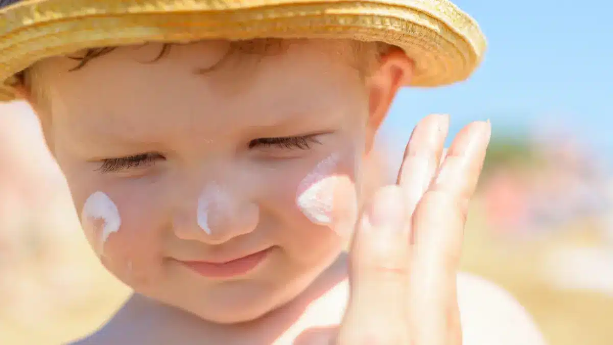 Mutter cremt Gesicht eines Kleinkinds mit Sonnencreme ein