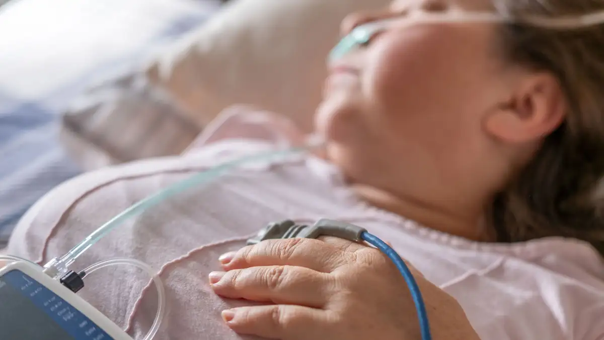 Frau liegt im Bett und ist mit verschiedenen medizinischen Geräten zur Schlafapnoe-Diagnose verkabelt.