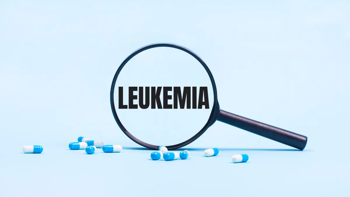 Schwarze Lupe auf hellblauem Hintergrund, im Glas steht gross das Wort LEUKEMIA, daneben liegen blau-weisse Kapseln als Symbolbild fuer Forschung zu akuter myeloischer Leukaemie