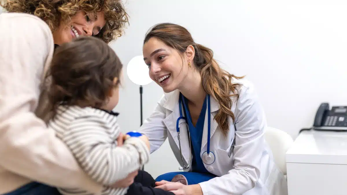 Kinderärztin untersucht Kleinkind, das am Schoß der Mutter sitzt