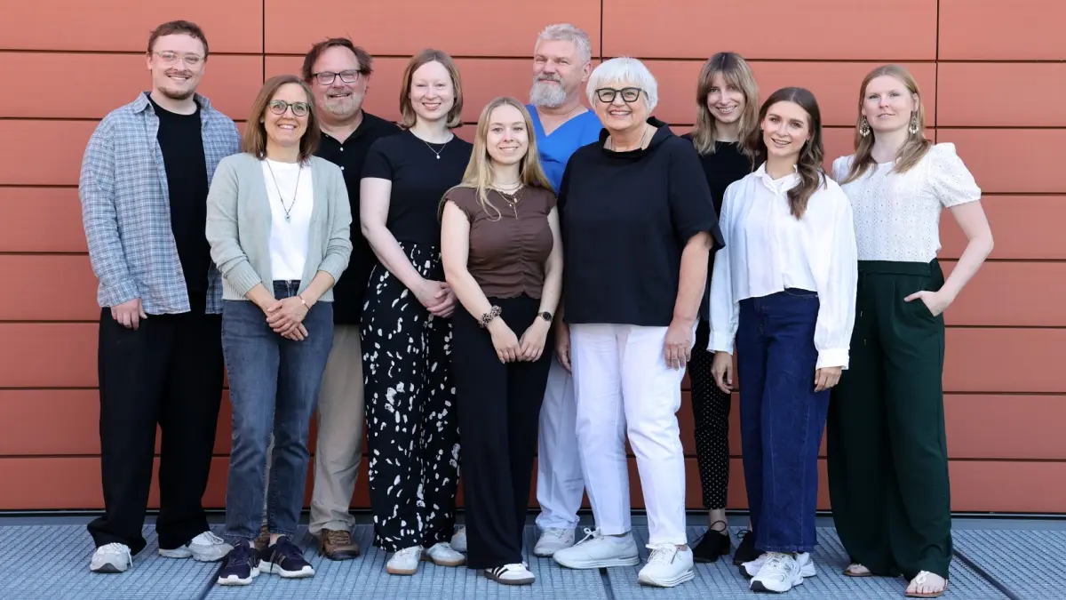 Gruppenfoto des Psychoonkologischen Dienstes am Universitaetsklinikum Regensburg mit zehn Mitarbeitenden vor roter Fassade zum Jubilaeum 25 Jahre psychoonkologische Unterstuetzung