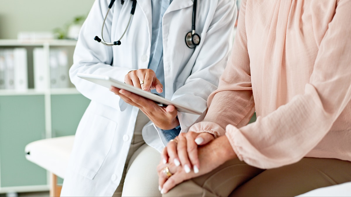 Arzt sitzt neben Patient und erklärt ihr etwas auf dem Tablet