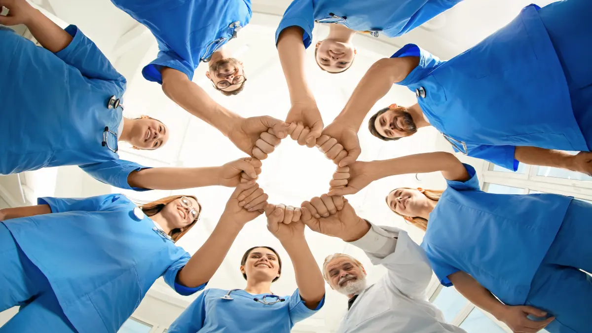 Medizinisches Team in blauer Klinikkleidung hält die Hände in der Mitte zusammen als Zeichen der Zusammenarbeit