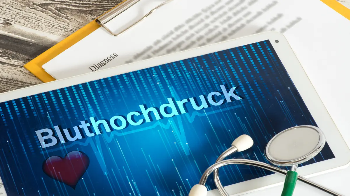 Tablet mit dem Schriftzug „Bluthochdruck“, daneben ein Stethoskop und Diagnoseunterlagen.