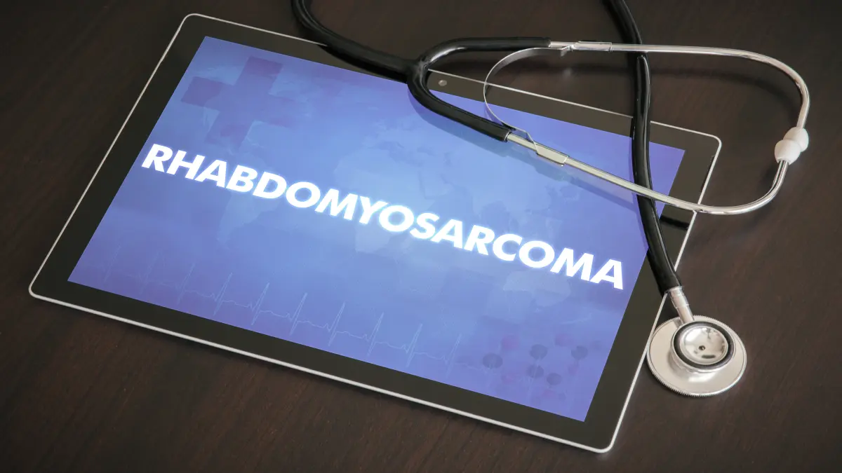 Tablet mit der leuchtenden Aufschrift RHABDOMYOSARCOMA und daneben ein Stethoskop auf dunkler Tischoberflaeche