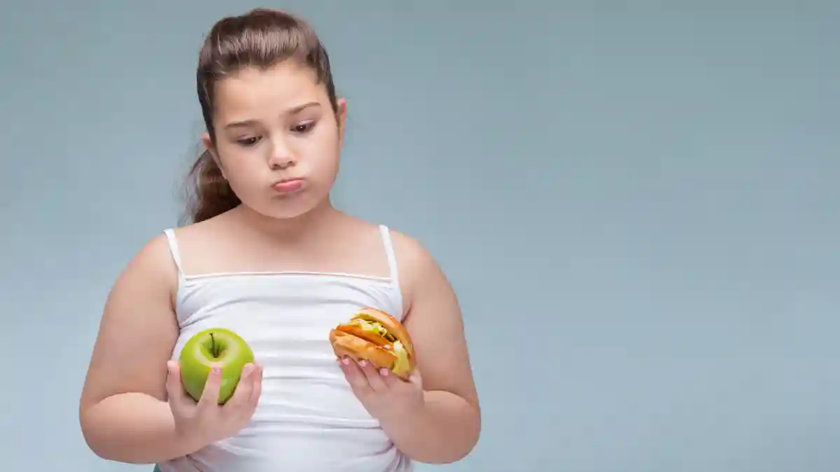 Bild eines jungen Mädchens, dass einen grünen Apfel in der einen Hand und einen Hamburger mit Schnitzel in der anderen Hand hält, das Kind sieht unsicher aus, welches es essen soll.