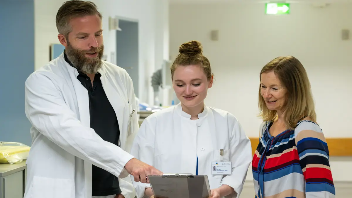Zwei Aerztinnen und Aerzte im weissen Kittel besprechen mit einer Frau ein Dokument auf einem Klemmbrett, Symbolbild fuer Beratung zur Krebsprävention beim Lynch-Syndrom