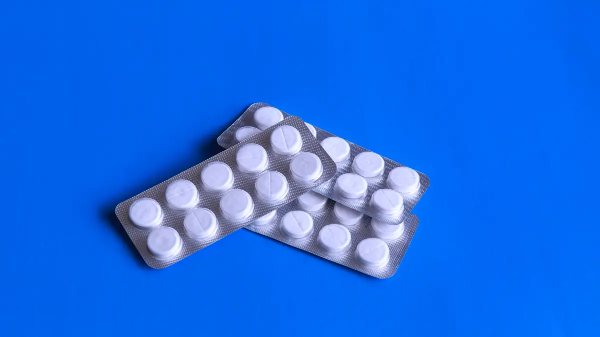 Zwei Blisterstreifen mit weißen Tabletten auf blauem Hintergrund.