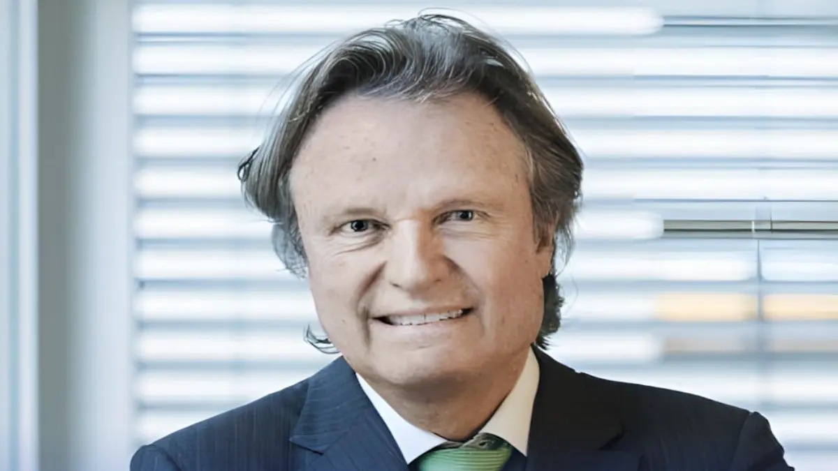 Porträt von Prof. Thomas F. Lüscher im dunklen Anzug mit grüner Krawatte vor einem Fenster mit Jalousien